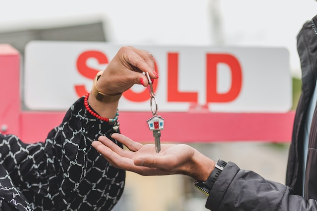 person passing house keys to someone else in front of a red sold sign